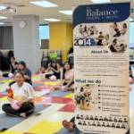 Screenshot 2569-08-12 at 161132 - The Balance Studio - T.092 2469 462 People seated on colorful exercise mats in a Pilates studio, with a tall banner for The Balance Pilates & Physio in the foreground.