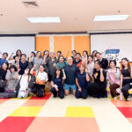 office syndrome workshop for employees 1 - The Balance Studio - T.092 2469 462 Group of people in a fitness studio posing for a photo, many with raised fists and smiles, colorful floor tiles behind them.